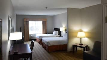 A hotel room with two beds, a desk, a chair, a lamp, and a window with curtains.