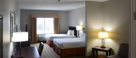A hotel room with two beds, a desk, a chair, a lamp, and a window with curtains.