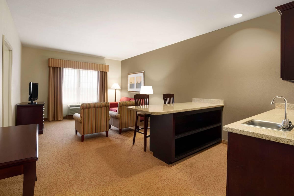 A compact hotel room with a kitchenette, a dining area, a sofa, and a television.
