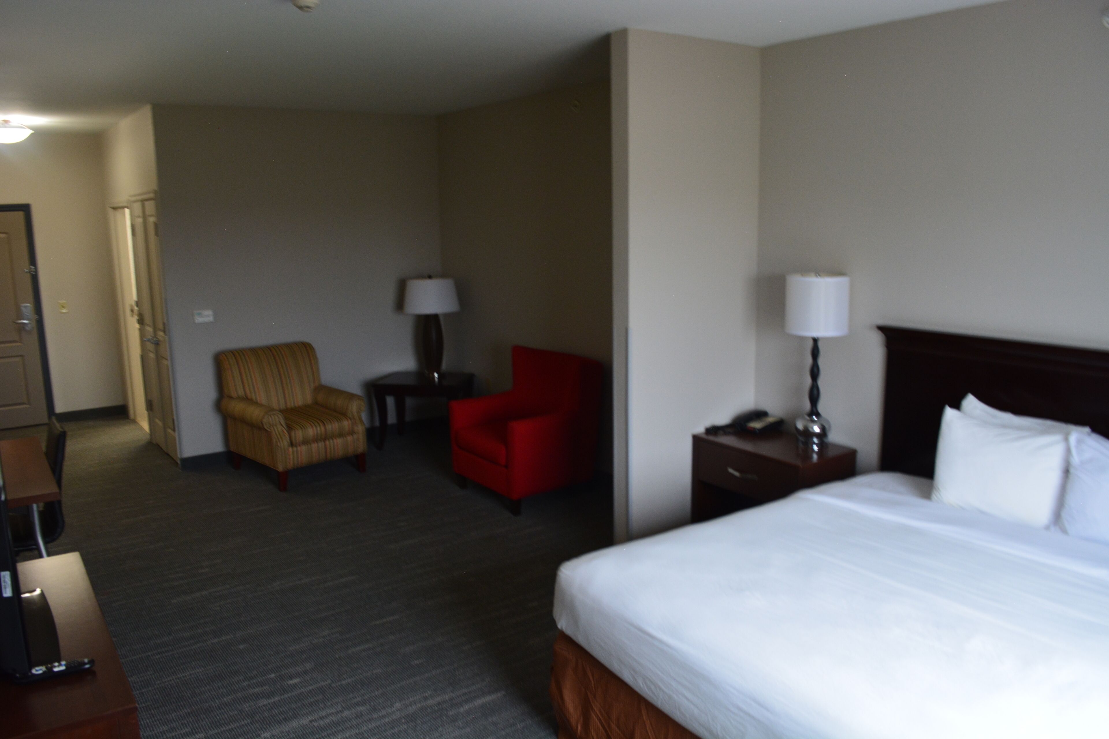 A hotel room with a large bed, a desk, a chair, and a lamp.