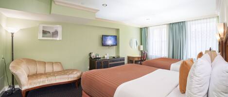A hotel room with two beds, a sofa, a desk, a television, and a window with curtains.