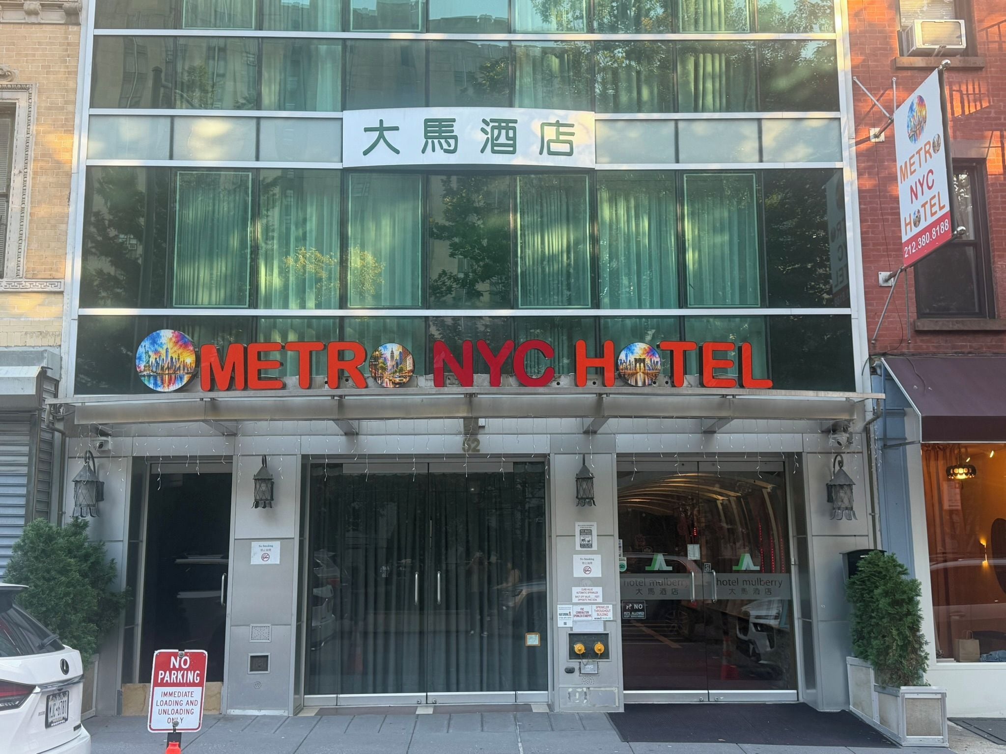 El exterior del Metro NYC Hotel, con una entrada despejada, señalización en varios idiomas y un letrero de no estacionamiento visible.
