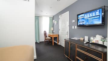 Habitación de hotel con una cama, un escritorio con una silla, un televisor montado en la pared y un armario con varios objetos encima.
