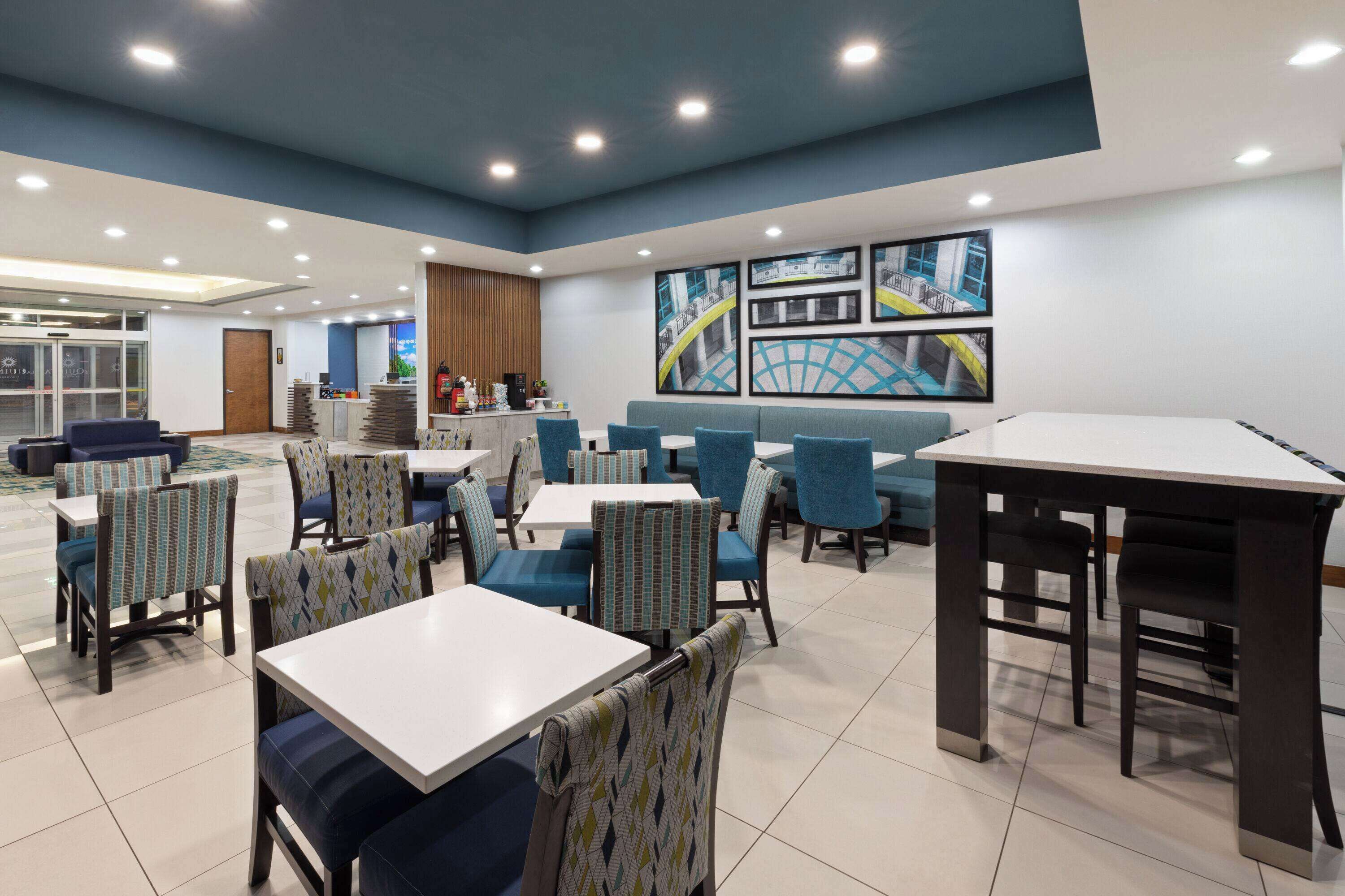 A modern dining area with multiple tables and chairs, a counter with a coffee machine, and a large wall mural.