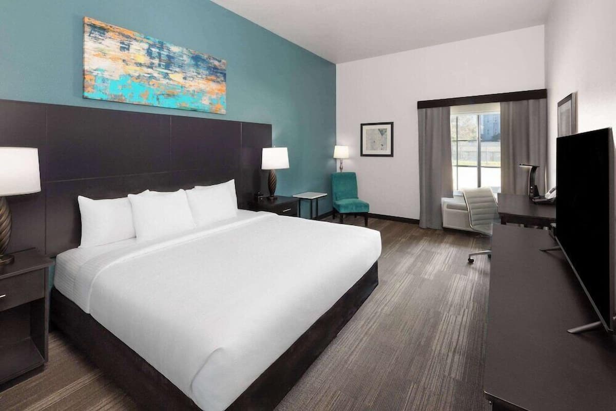 Una habitación de hotel con una cama grande, un escritorio, una silla, un televisor y obras de arte en las paredes.