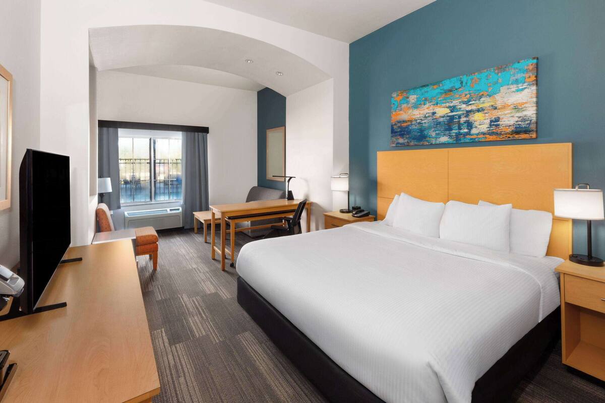 Habitación de hotel con una cama grande, un escritorio, una silla, un televisor y una ventana con cortinas.