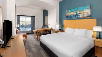 Habitación de hotel con una cama grande, un escritorio, una silla, un televisor y una ventana con cortinas.