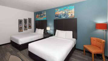 A hotel room with two beds, a chair, and artwork on the walls.
