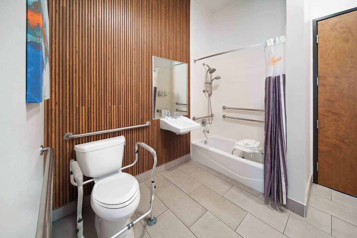 Un baño moderno con pared de paneles de madera, un lavabo blanco, un inodoro con elevador para silla de ruedas y una ducha a nivel.