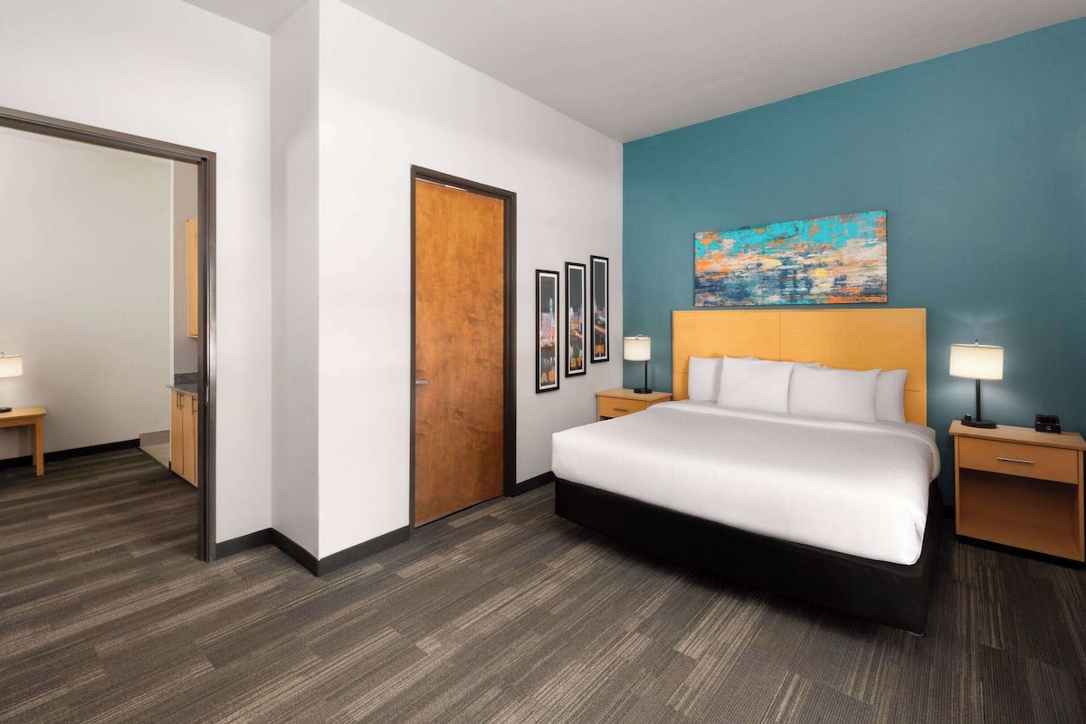 Una habitación de hotel con una cama grande, una puerta de madera, un muro azul decorativo y cuadros en la pared.