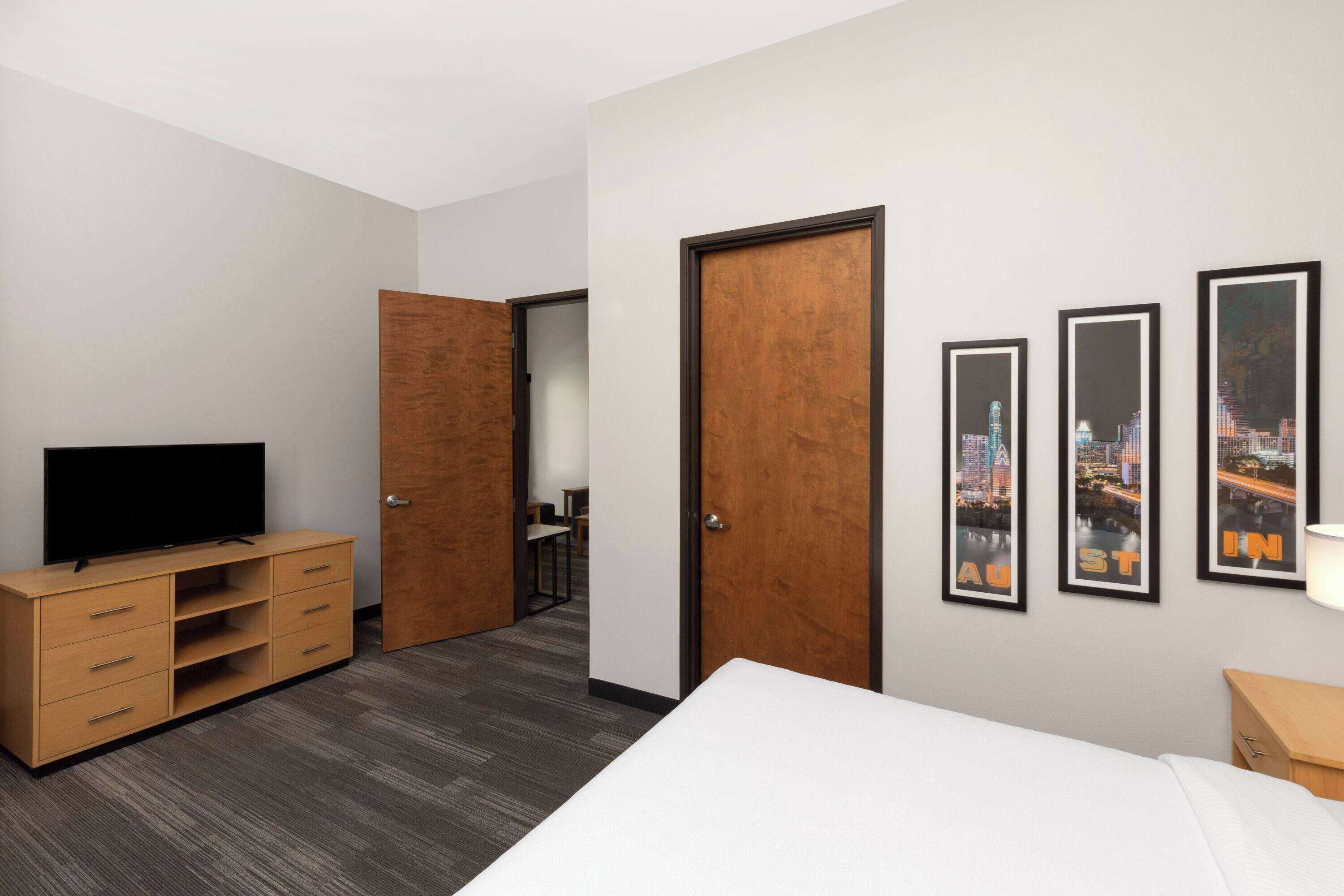 A hotel room with a bed, a TV, a wooden wardrobe, a desk, and a chair.