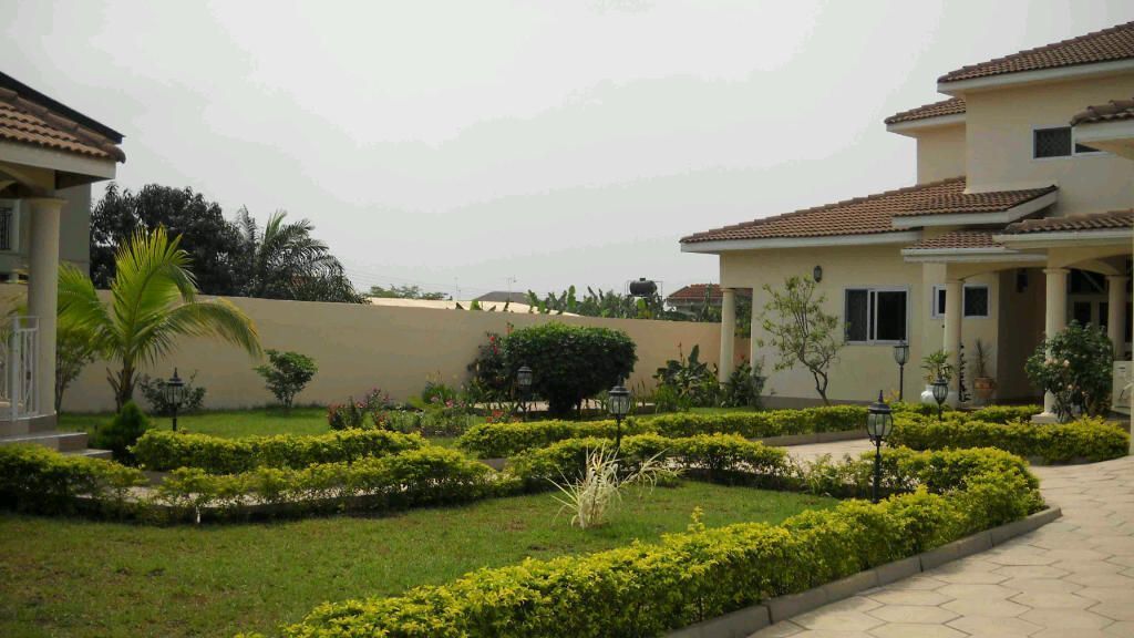 A residential area with two houses, well-maintained gardens, and a paved pathway.