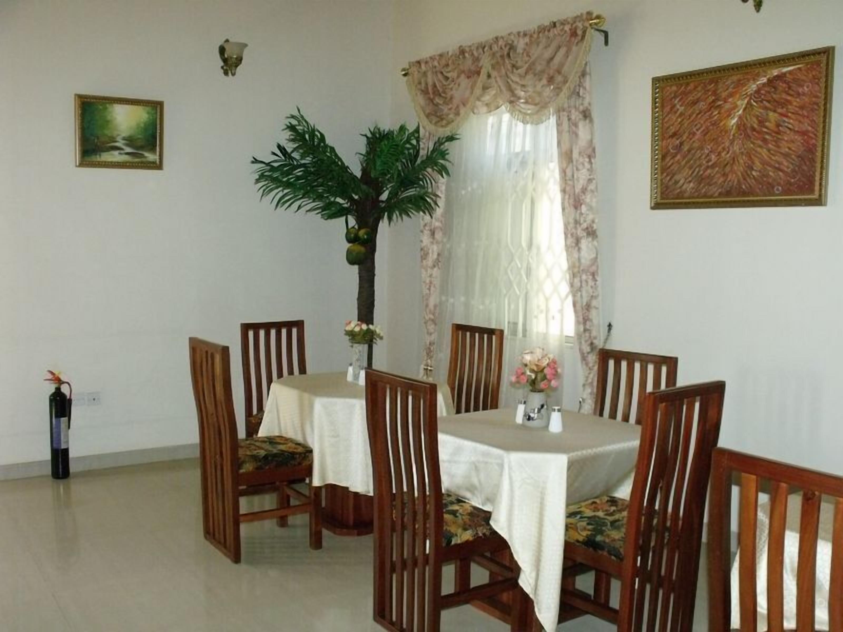 Une salle à manger avec une table ronde, six chaises en bois, une plante en pot et deux tableaux accrochés au mur.