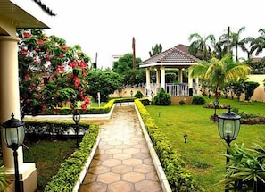 A garden pathway leading to a gazebo with a tiled roof, surrounded by well-maintained hedges and tropical plants. - Acacia Lodge, North Legon (Kwabenya)