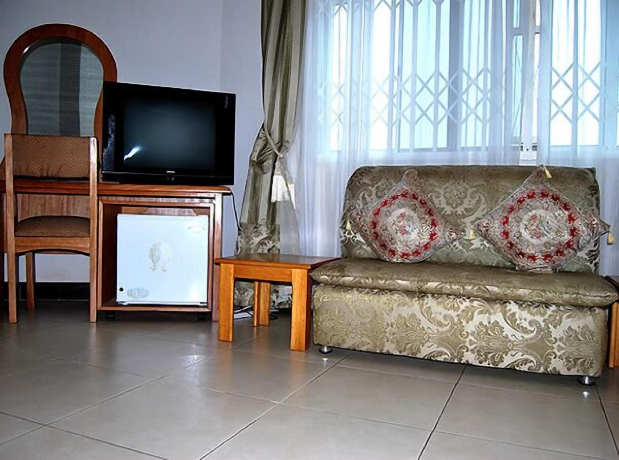 A living room with a television on a wooden stand, a sofa with patterned cushions, and a small table.
