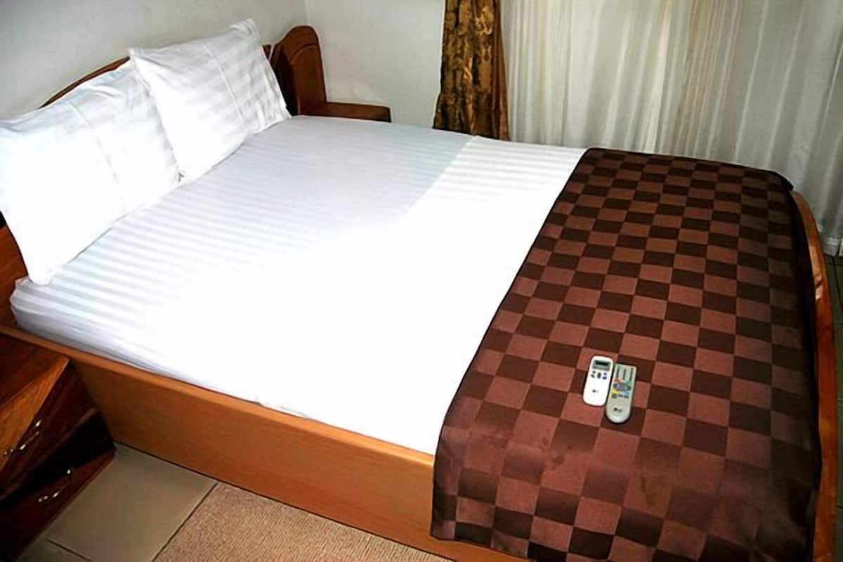 A hotel room with a bed, a checkered blanket, and a remote control on the bed.