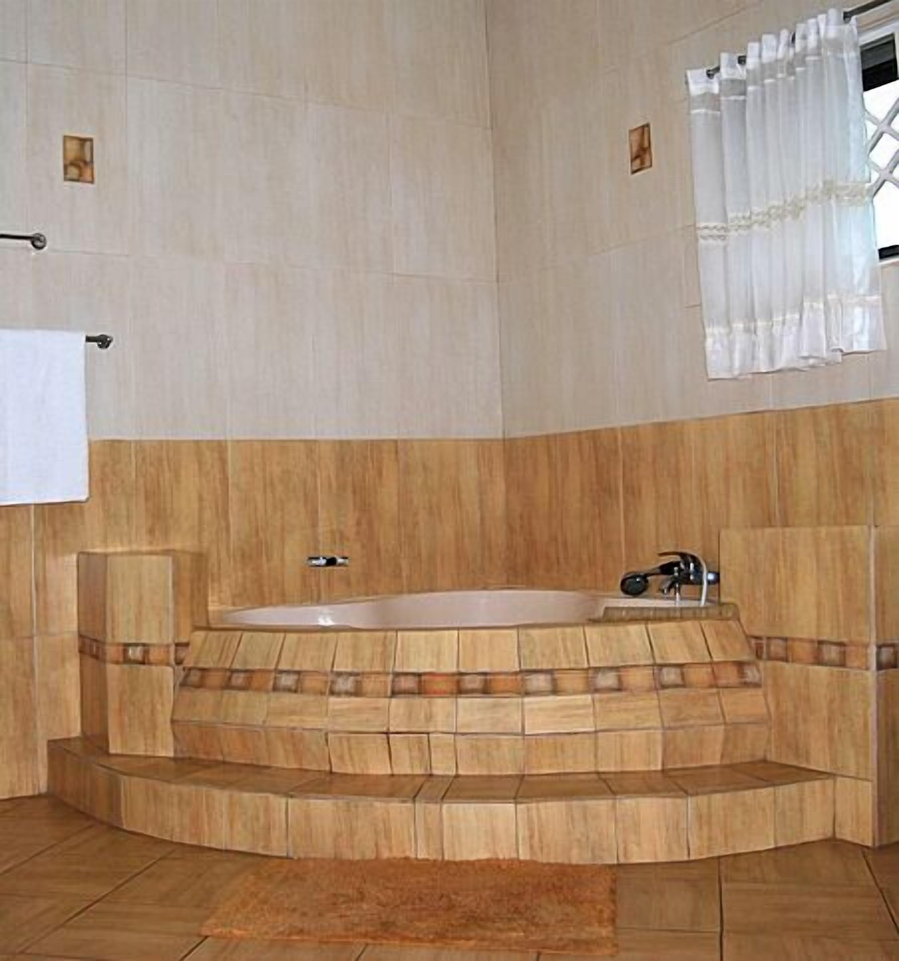 Ein Badezimmer mit einer freistehenden Badewanne, Holzvertäfelung und einem Fenster mit weißen Vorhängen.