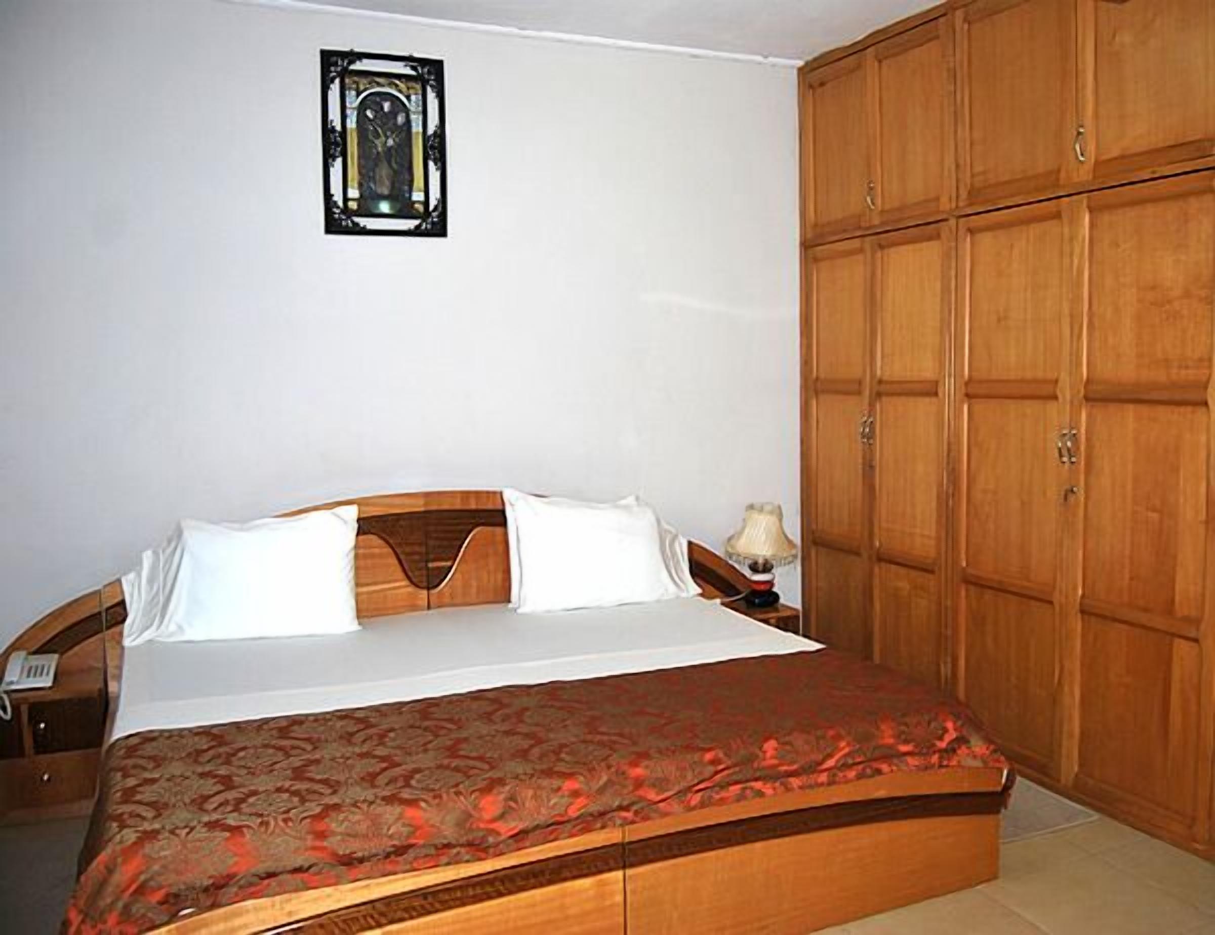 A bedroom with a bed, a nightstand, a lamp, and a wooden wardrobe.