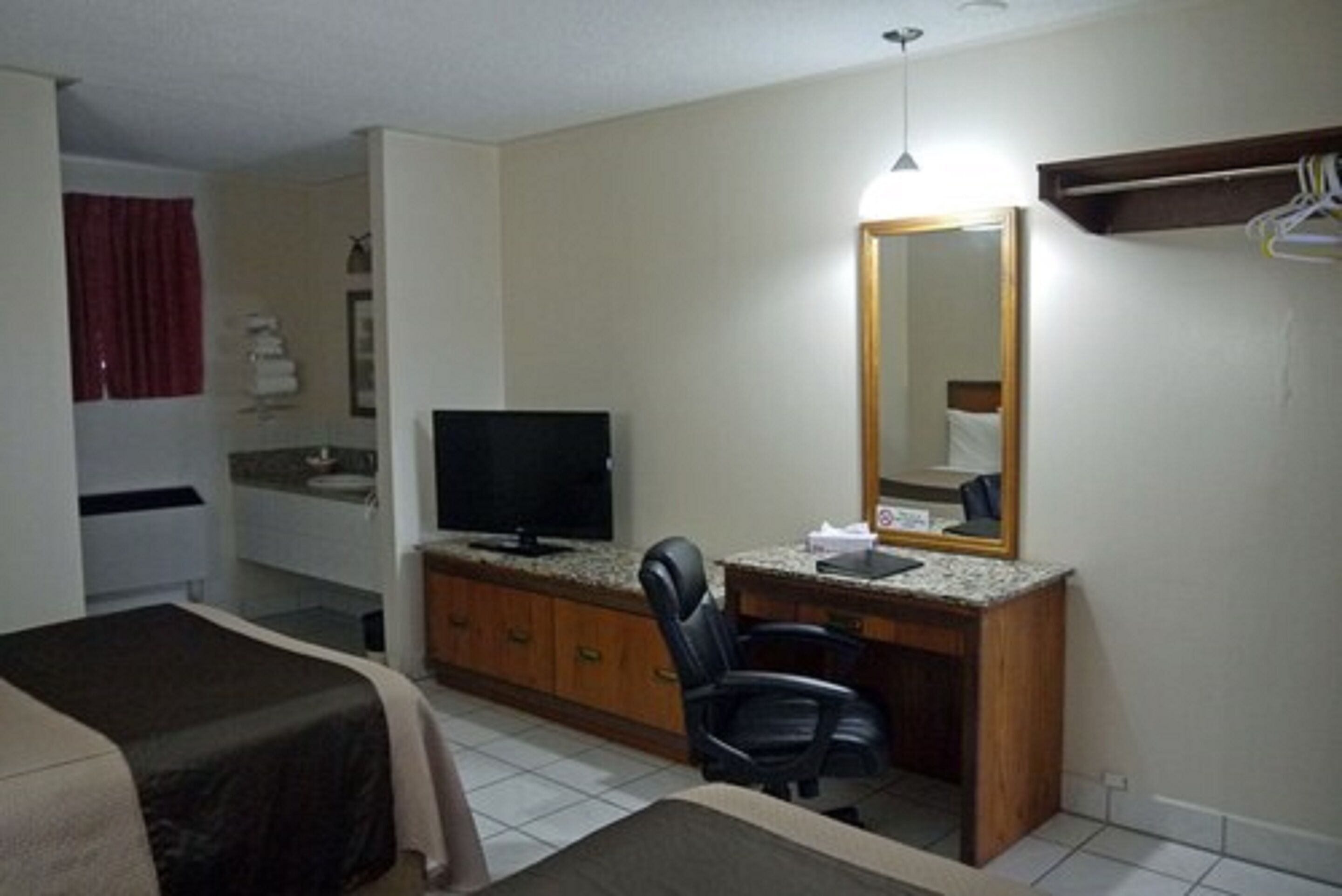 Une chambre d’hôtel avec un lit, un bureau et une chaise, une télévision, un miroir et une salle de bain visible au fond.