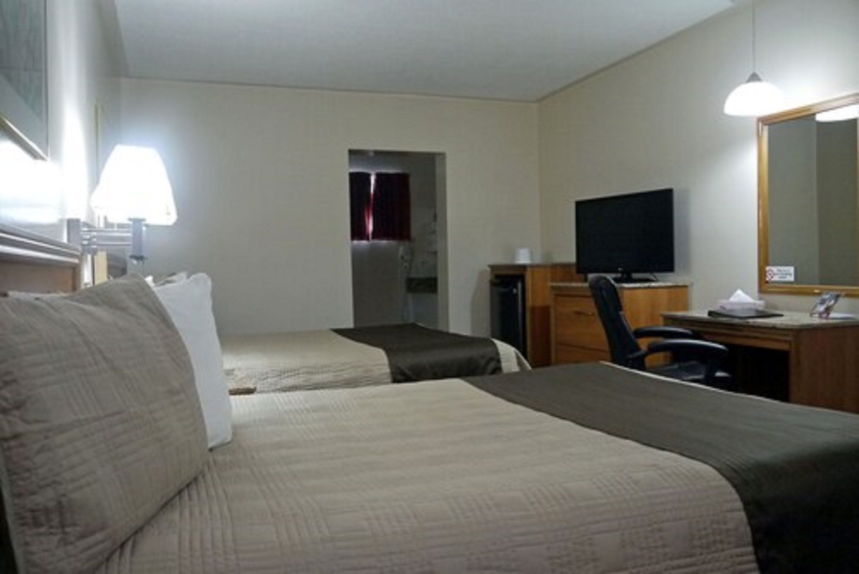 A hotel room with two beds, a desk, a television, and a mirror.