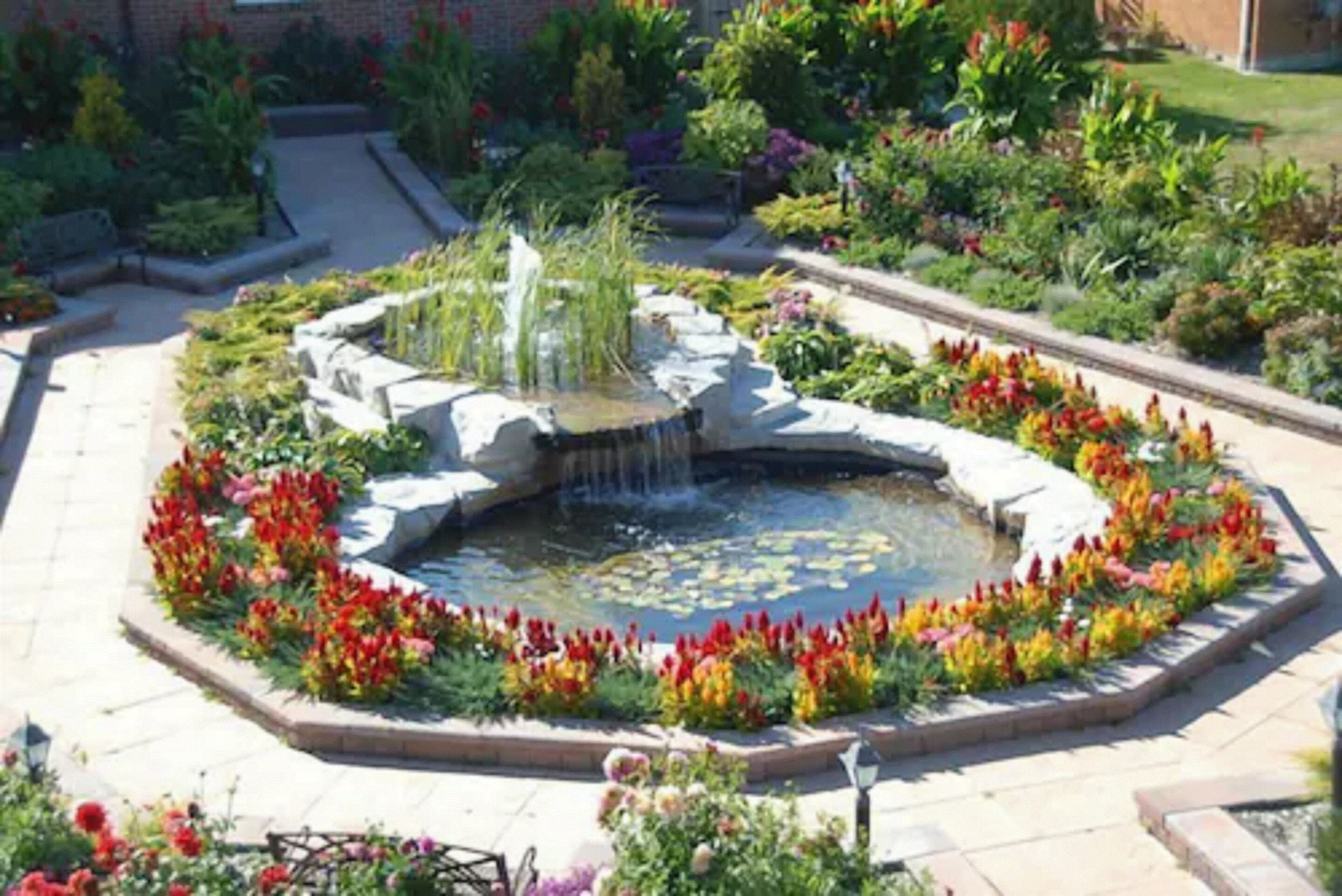Un jardín circular con una fuente central rodeada de flores y plantas coloridas.