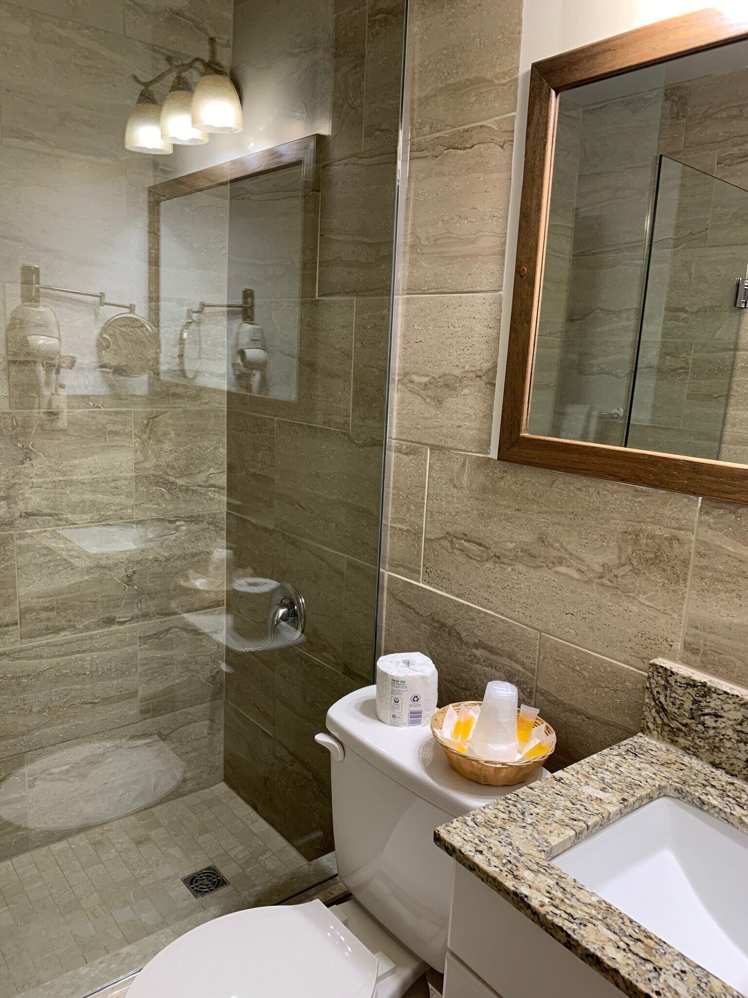 A modern bathroom with a glass-enclosed shower, a toilet, and a sink with a granite countertop.