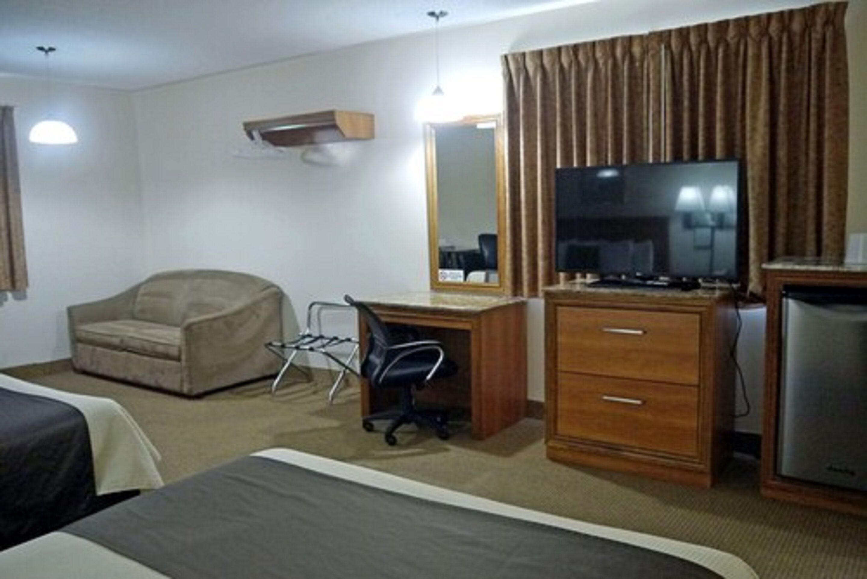 Una habitación de hotel con cama, escritorio con computadora, silla, televisor y refrigerador.
