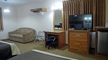 Una habitación de hotel con cama, escritorio con computadora, silla, televisor y refrigerador.