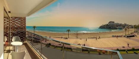 Uma varanda com vista para uma praia e um edifício ao longe.