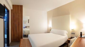 Habitación de hotel con cama, mesita de noche, lámpara y armario de madera.