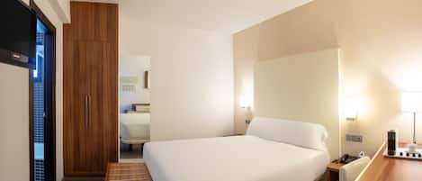 A hotel room with a bed, bedside table, lamp, and a wooden wardrobe.