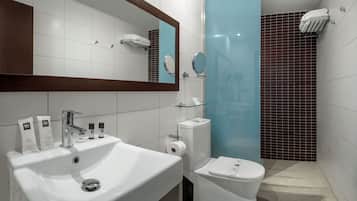 Un baño moderno con un lavabo blanco, espejo y retrete. Hay artículos de aseo en el lavabo y un estante de vidrio sobre el retrete.