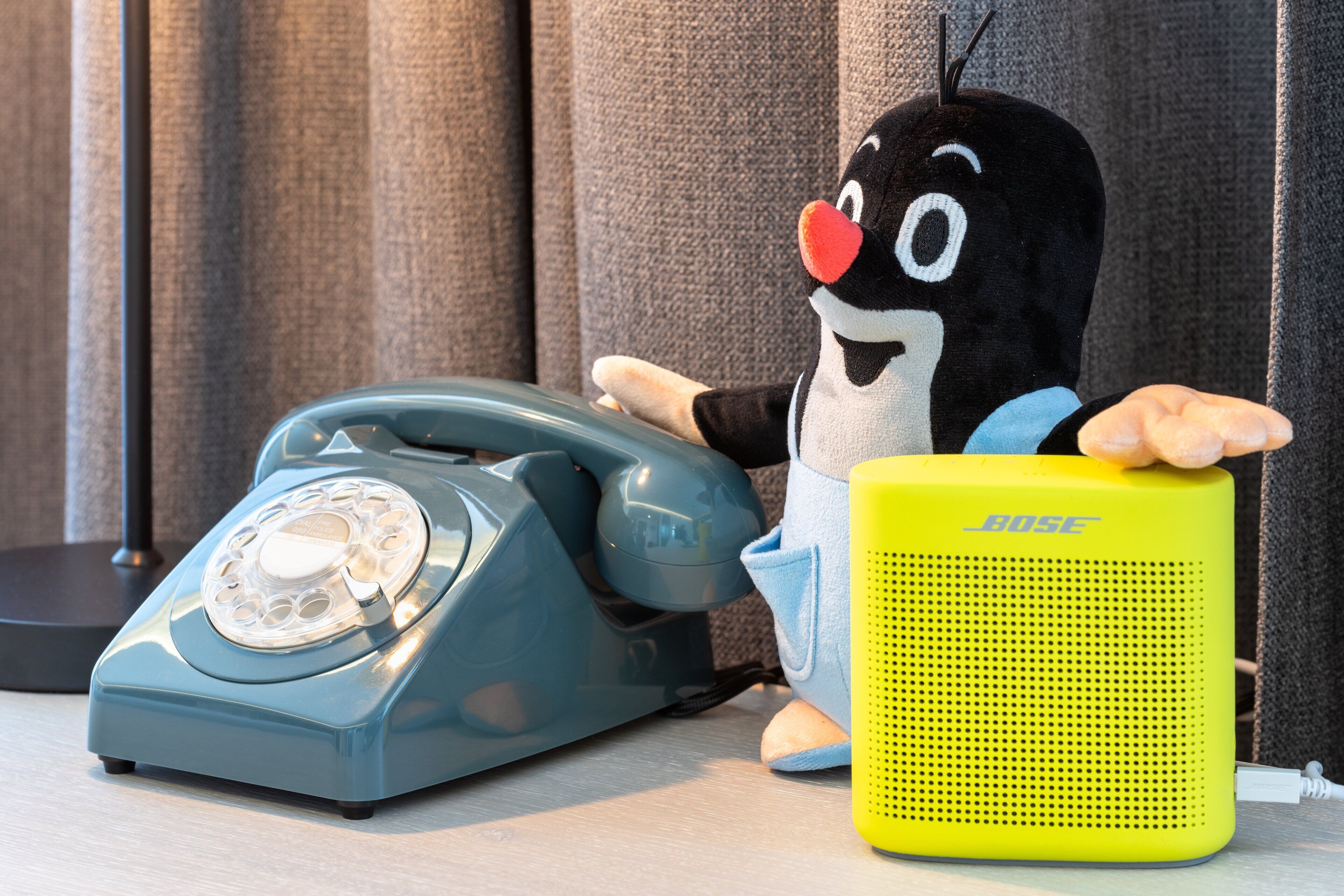 A vintage telephone, a plush toy, and a yellow speaker on a table.