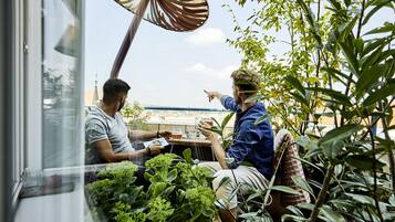 Deux personnes sont assises à une table, entourées de plantes, avec une vue sur la ville.