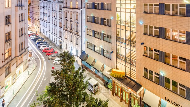 A hotel with a modern facade, a visible staircase, and a street view with parked cars.