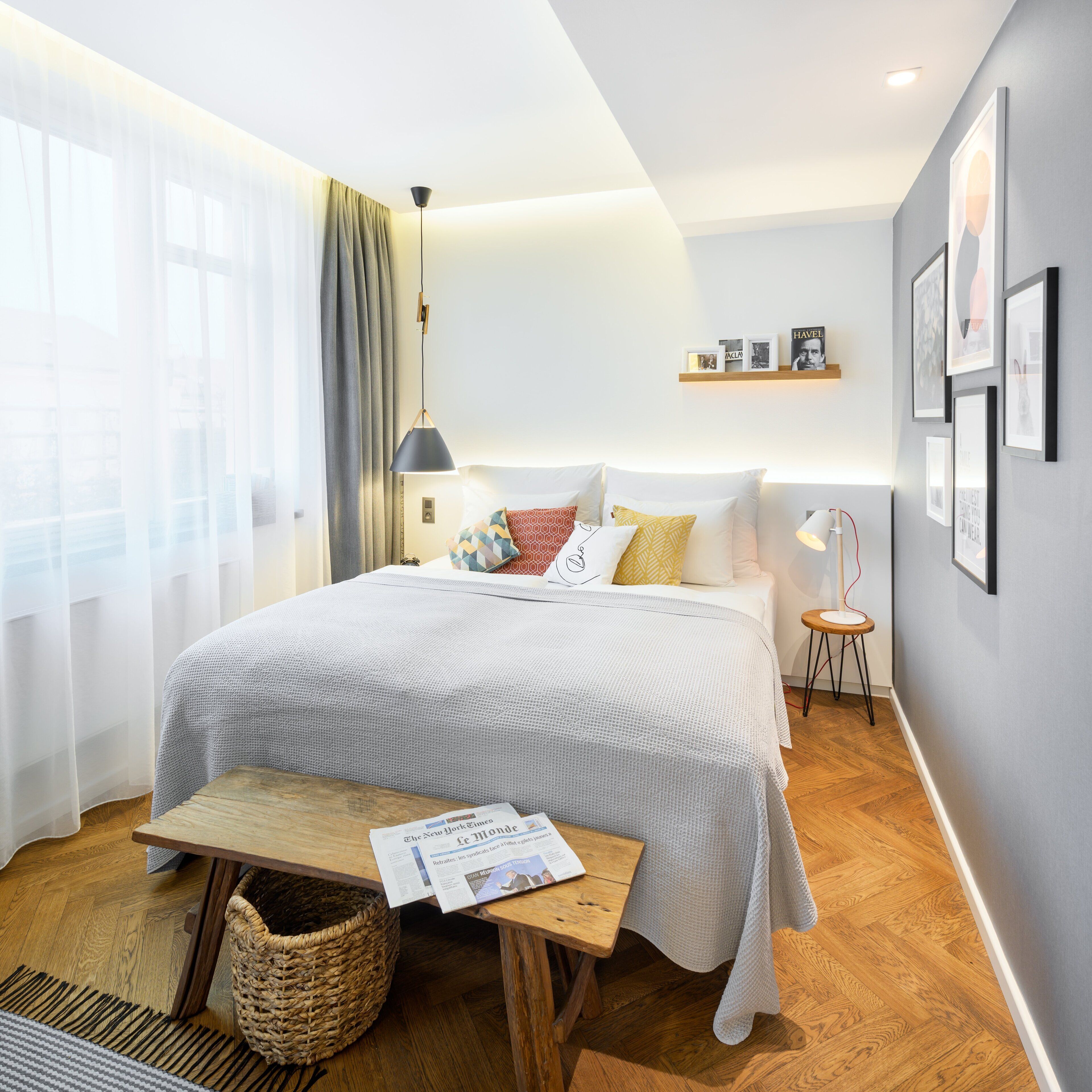 Un dormitorio moderno con una cama grande, mesitas de noche, una lámpara de lectura y una pequeña mesita auxiliar.
