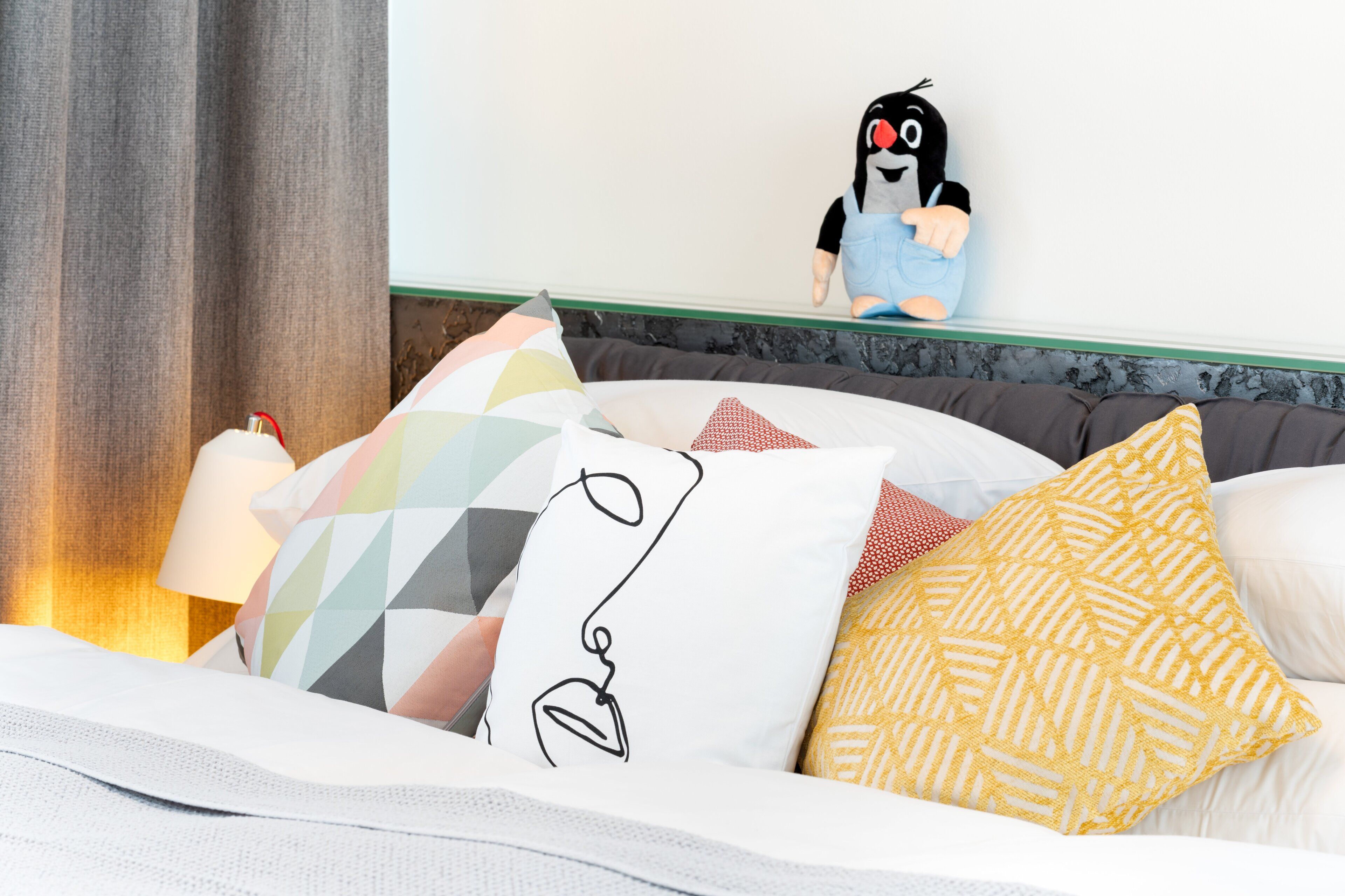 A bed with multiple pillows, a lamp, and a plush toy on the headboard.