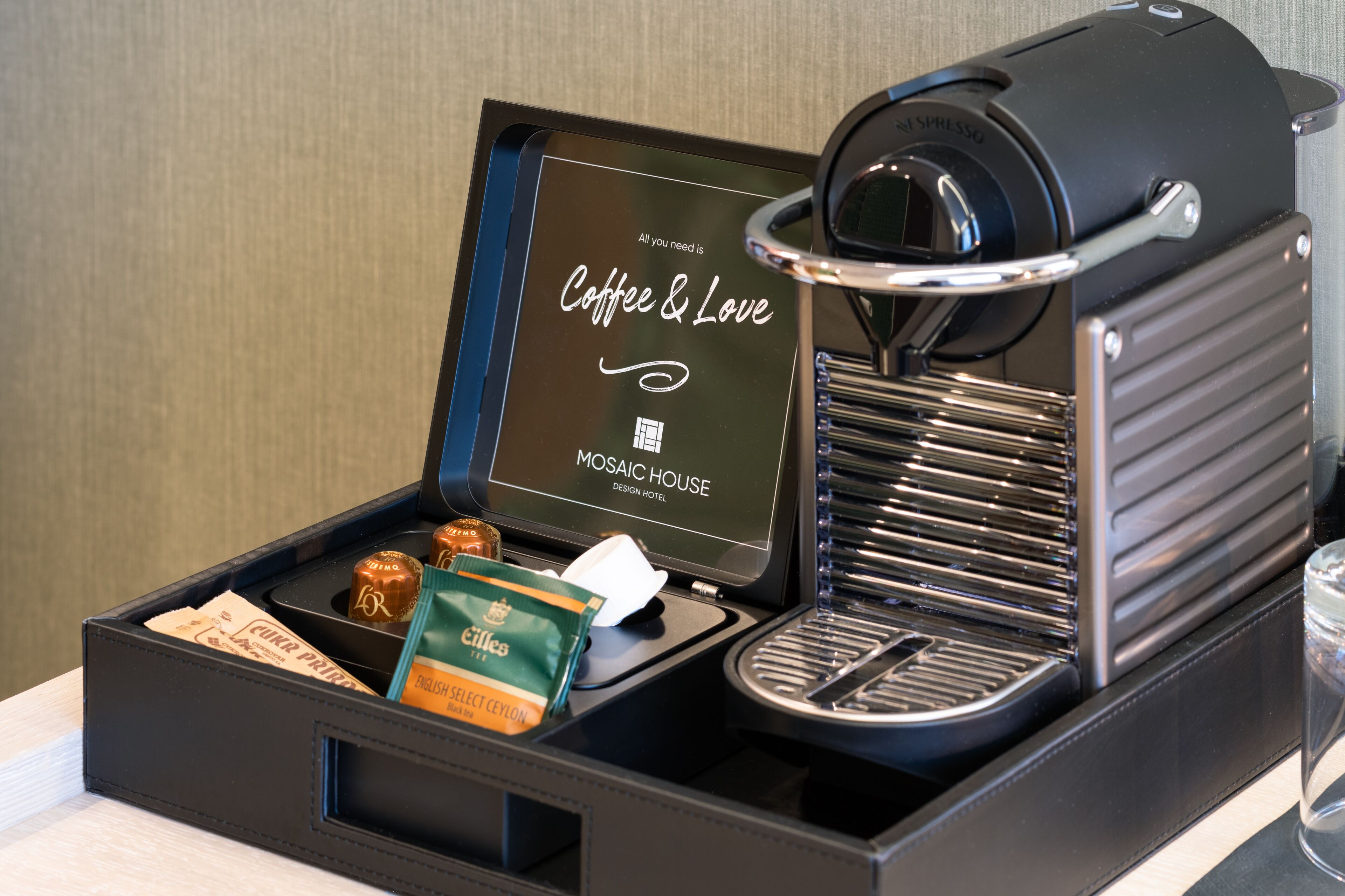 Una cafetera con pantalla, una bandeja con cápsulas de café y un vaso de agua.