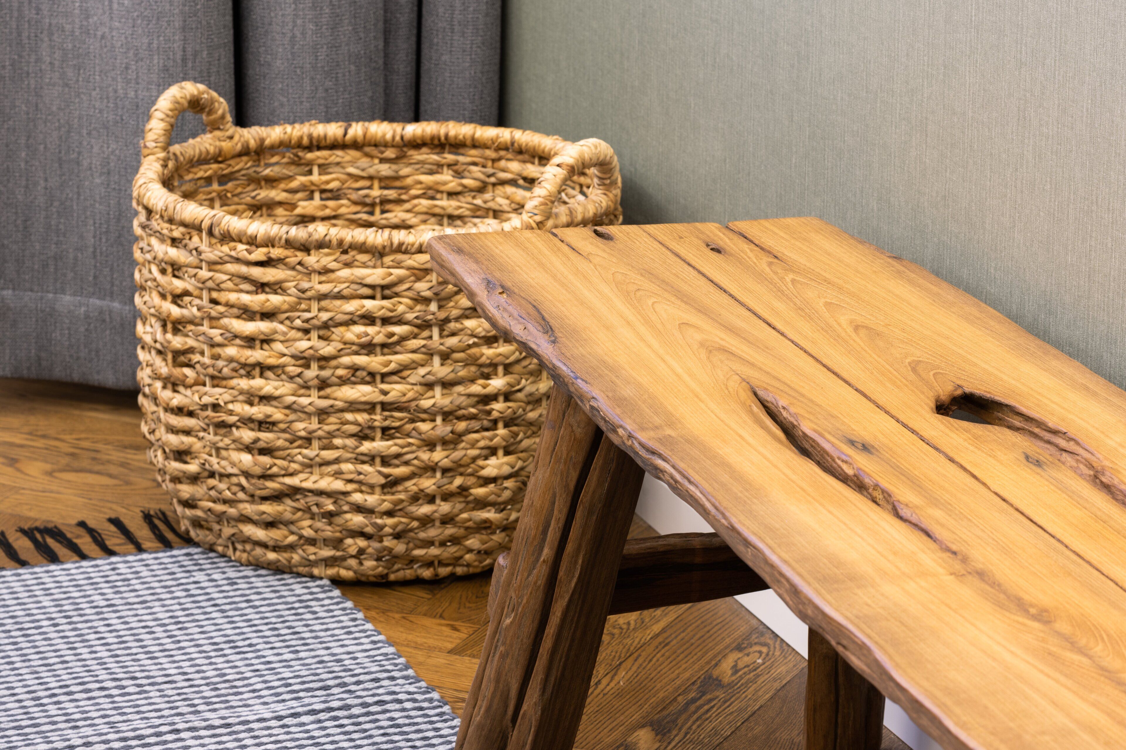 Una cesta tejida y una mesa de madera con un diseño recortado, sobre un suelo de madera con un tapete estampado.