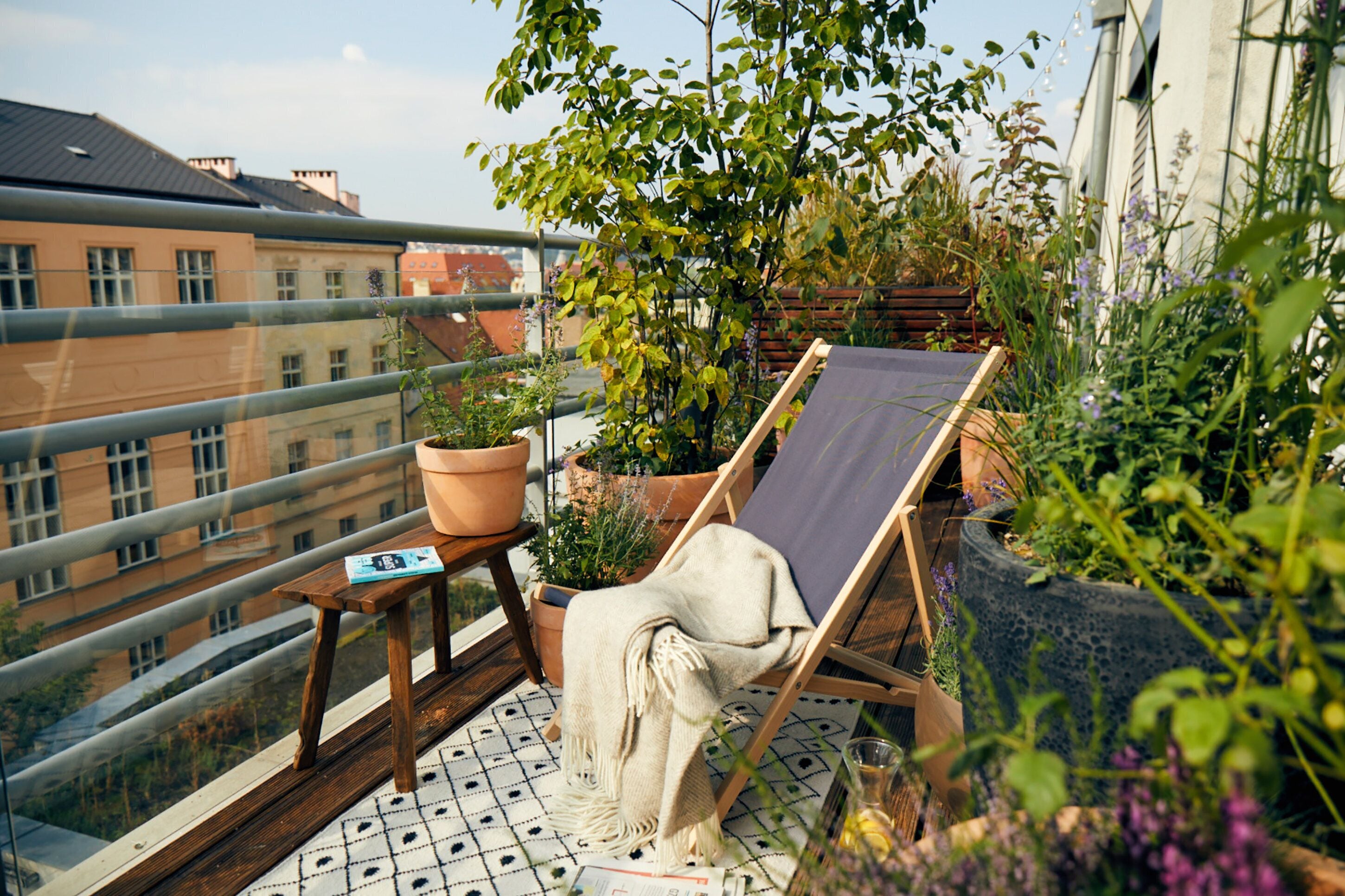 Un balcón con una silla de madera, una mesita y plantas en macetas.