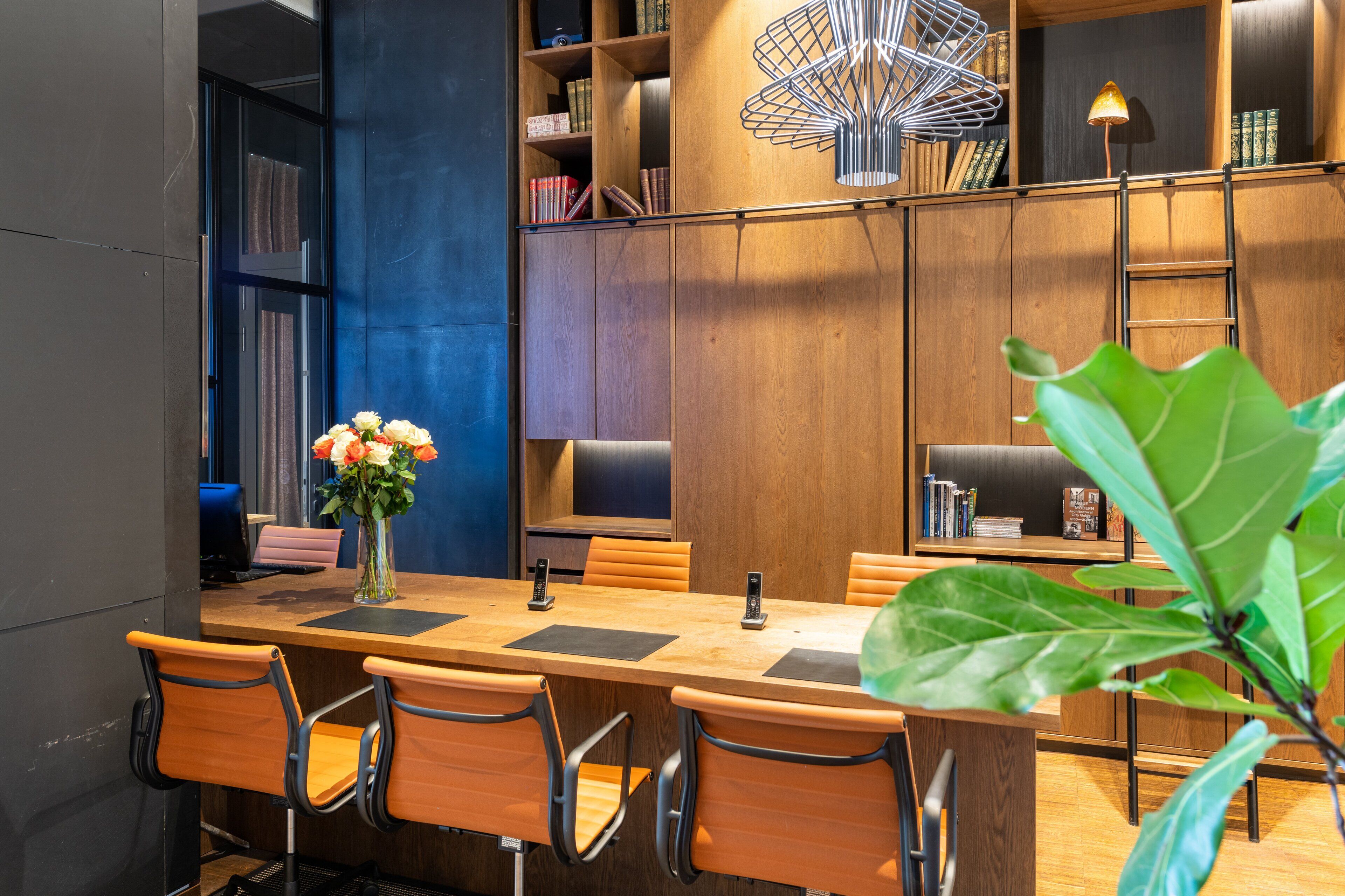 Uma sala de reuniões moderna com mesa de madeira, cadeiras, um vaso com flores e estantes cheias de livros e objetos decorativos.