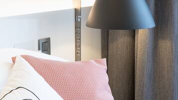 Una cama bien tendida con almohadas estampadas, una lámpara de noche y un cartel en la pared que dice 'HOUSE'.