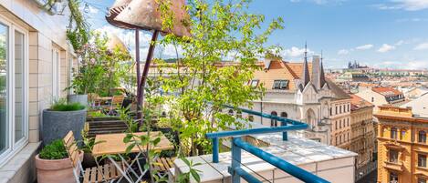 A rooftop terrace with potted plants, outdoor seating, and a view of the cityscape.