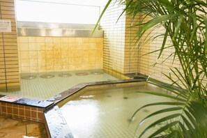 Un petit espace aménagé avec un jacuzzi carrelé, une rambarde en métal et une plante au premier plan.