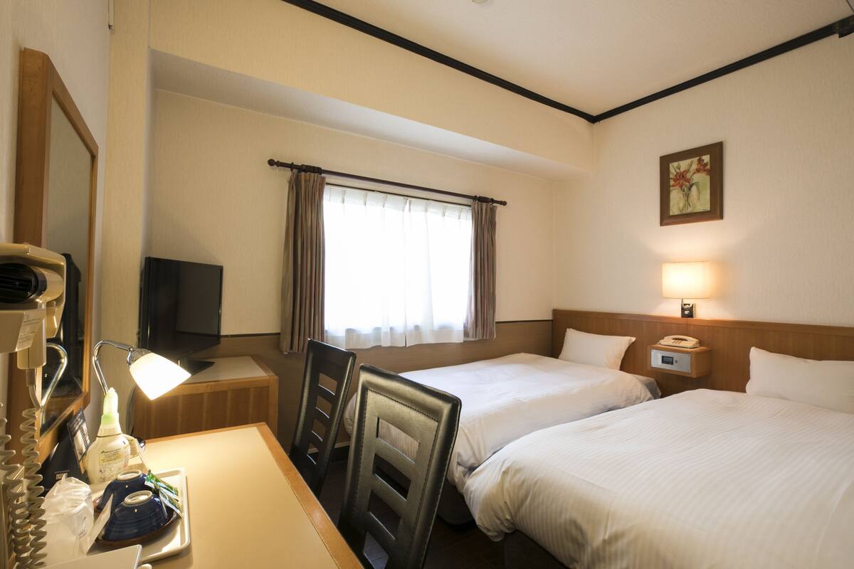 Habitación de hotel con dos camas, un escritorio con lámpara, teléfono y ventana con cortinas.