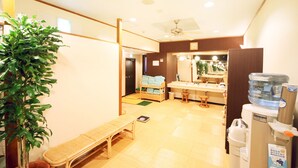 Habitación de hotel con piso de madera, un banco, dispensador de agua y una mesita.