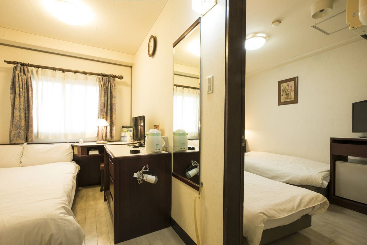 Habitación de hotel con dos camas, un escritorio, un espejo y un televisor.