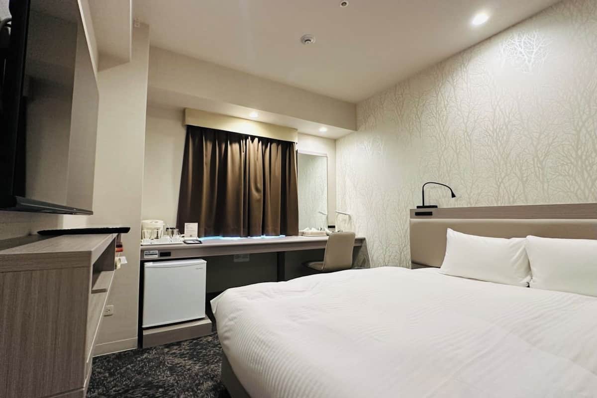 A hotel room with a bed, desk, chair, and a television.