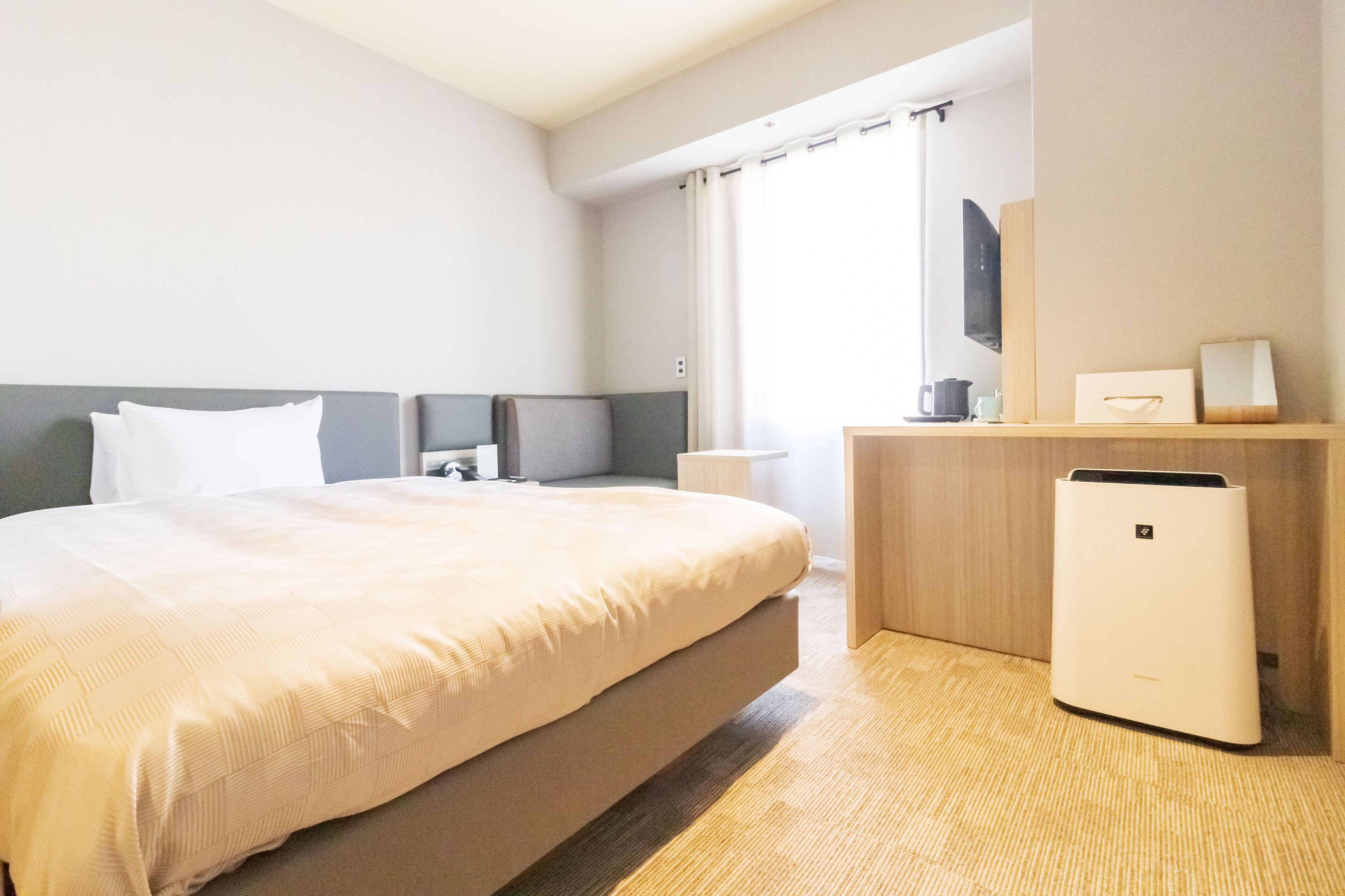 Et hotelværelse med en stor seng, et natbord, et lille skrivebord, en lampe og en varmeblæser.