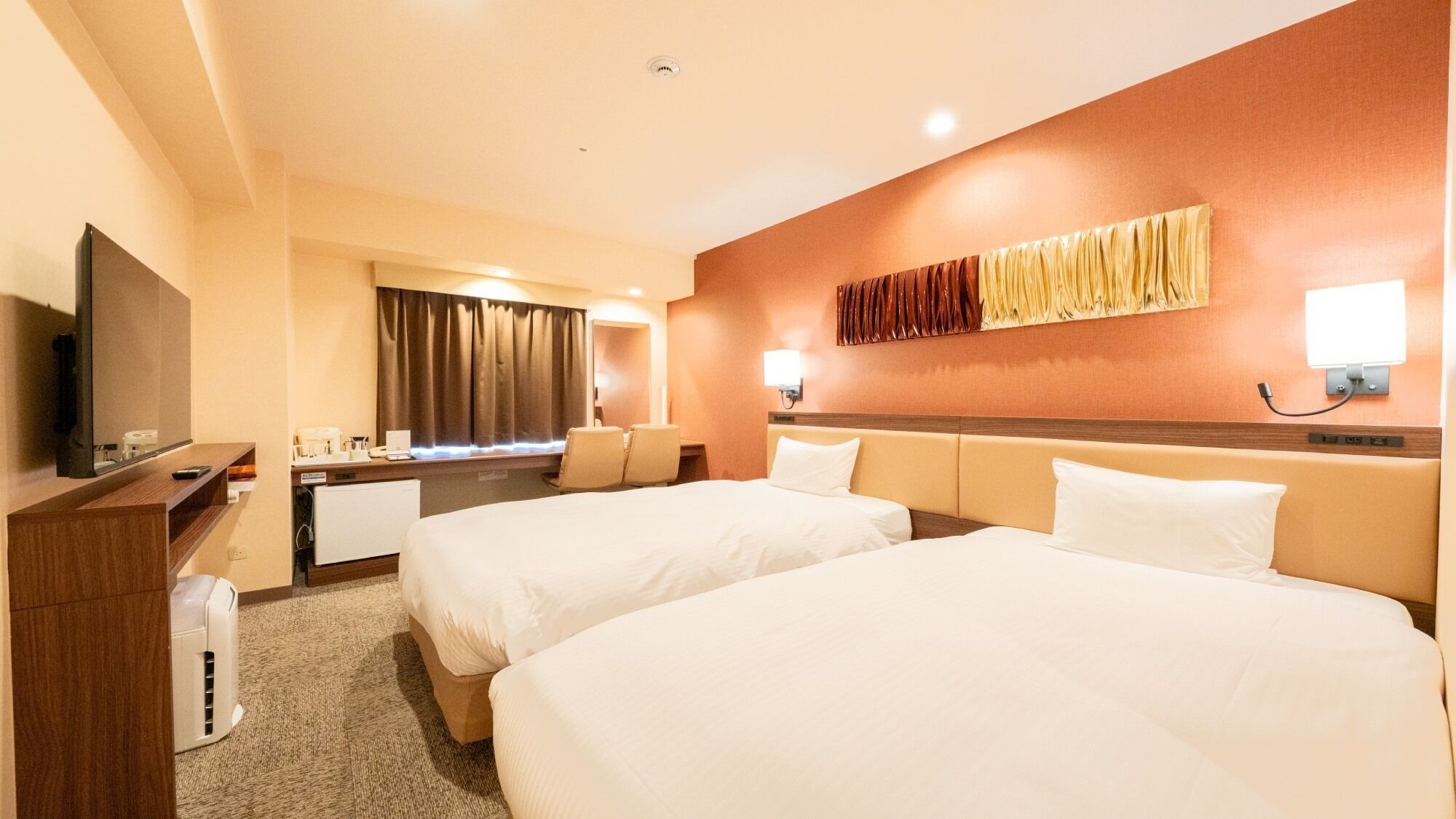 Hotelkamer met twee bedden, een bureau met een flatscreen-tv, een bureaulamp en een wandlamp.